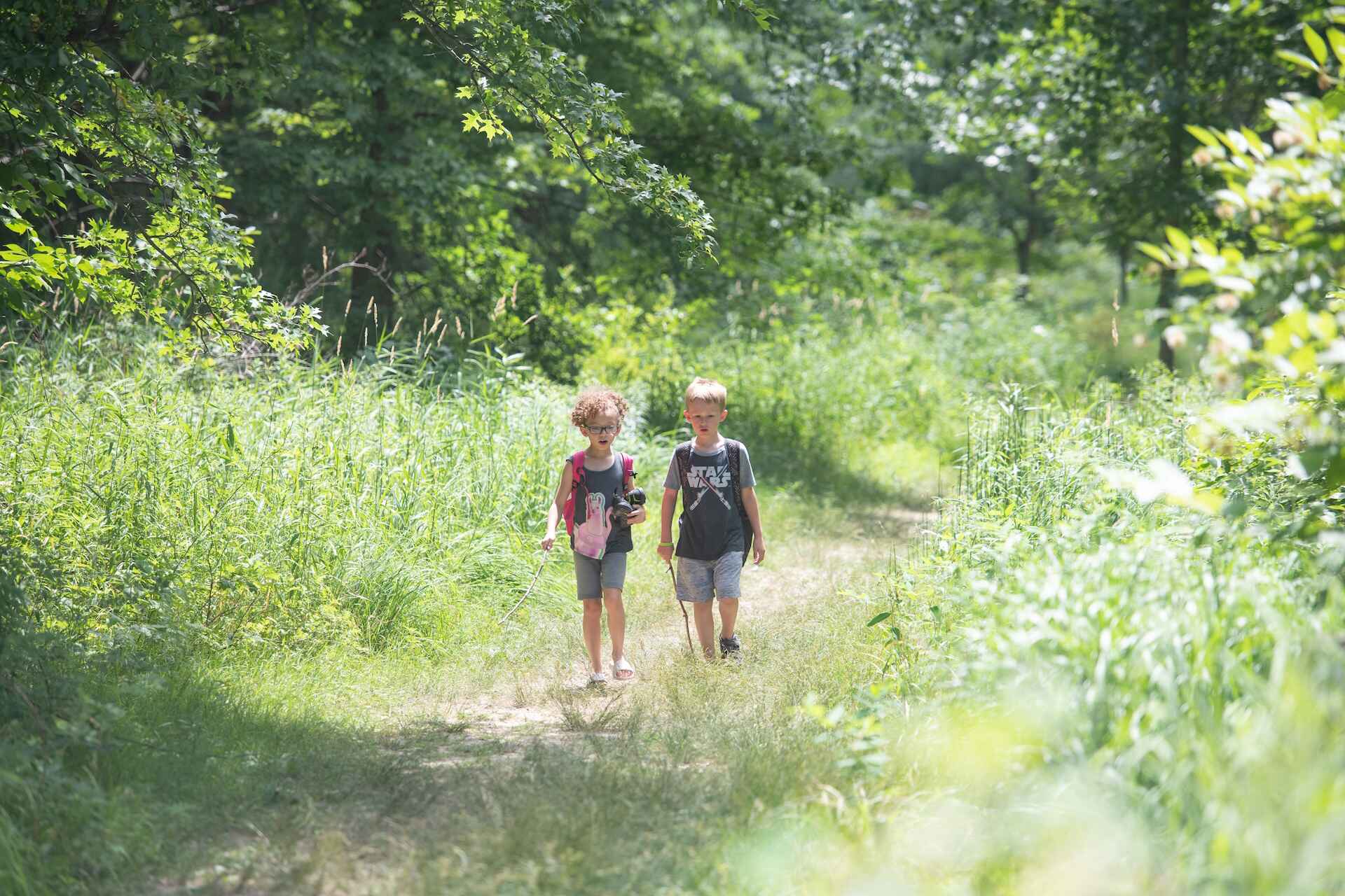 Two kids walking on a path inbetween grass 