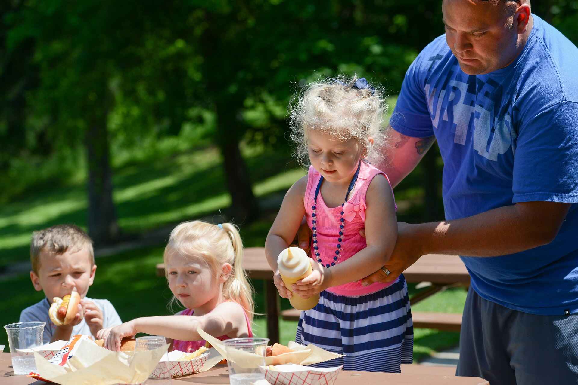 Man and kids eating hot dogs outside at a picnic table
