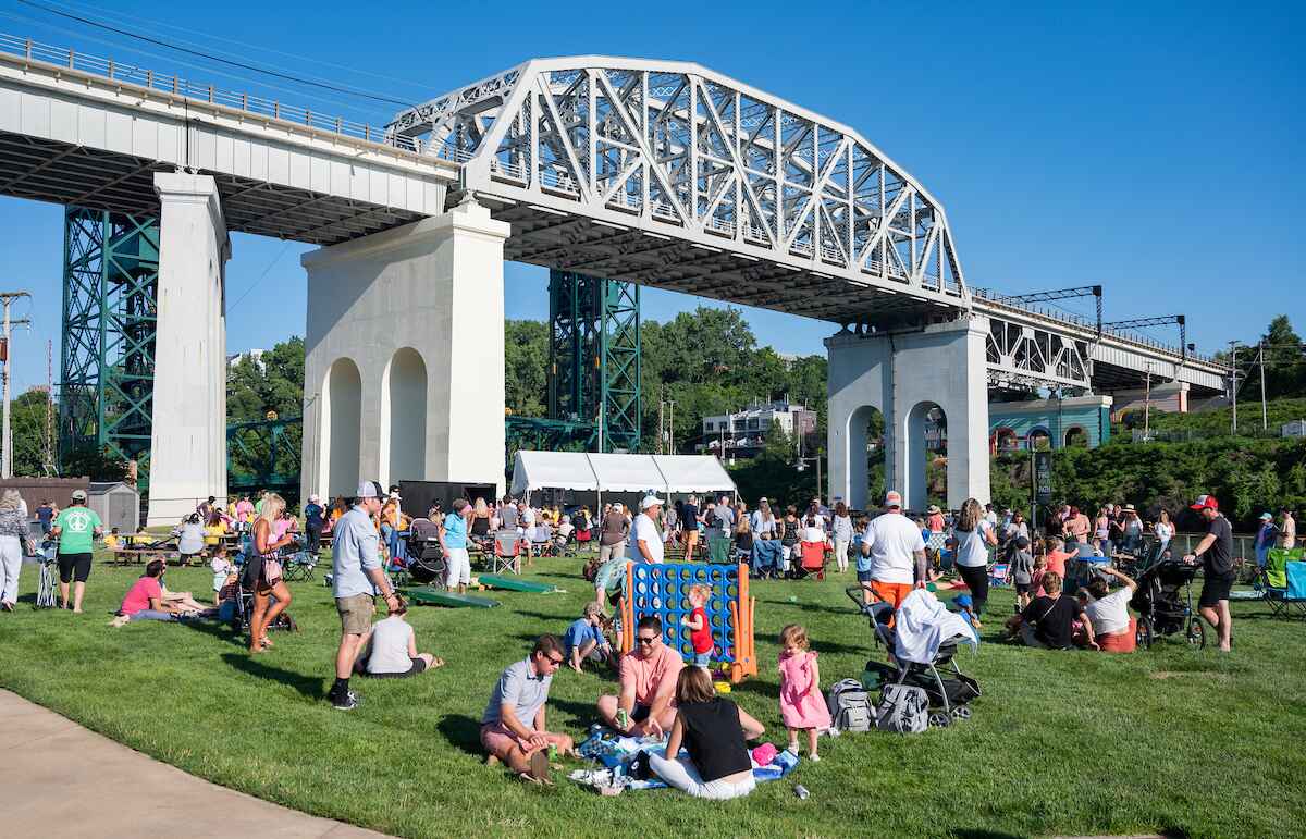 People hanging out in the grass underneath a bridge