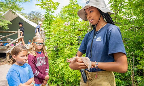 Photo of camp counselor holding snake with campers