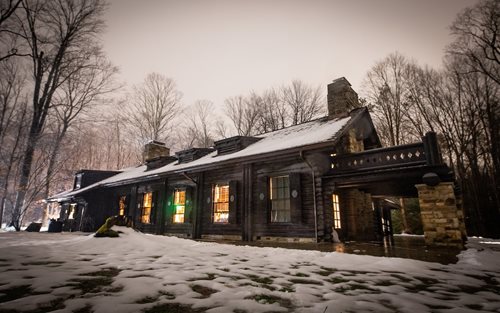 A spacious black house nestled among trees in the woods, shrouded in darkness, with a mysterious nighttime ambiance.