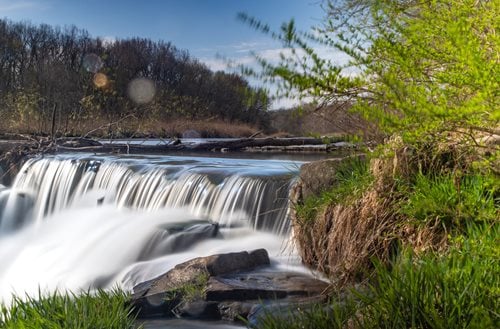 arafed waterfall with water flowing over rocks and grass, a tilt shift photo by Mike Bierek, instagram contest winner, hudson river school, a river flowing with waterfall, long exposure photography, peaceful beautiful waterfall