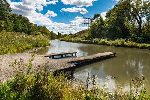A rustic wooden dock juts out into a tranquil river, framed by trees and reflecting the peaceful atmosphere of nature.