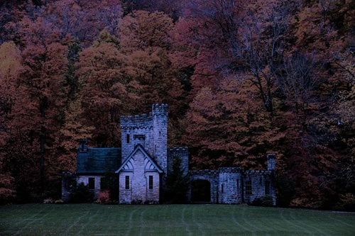 An ancient castle stands majestically in a vast, open field, surrounded by greenery and a clear blue sky.