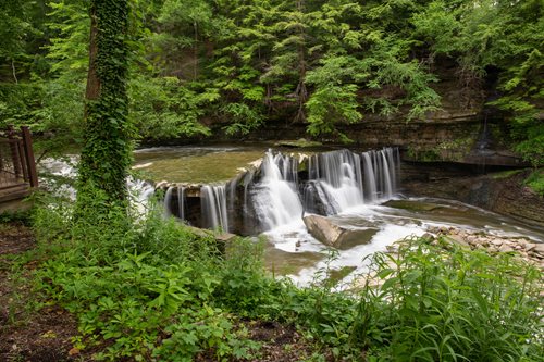 A picturesque waterfall surrounded by dense woods, with a wooden walkway providing access to the stunning natural landscape.