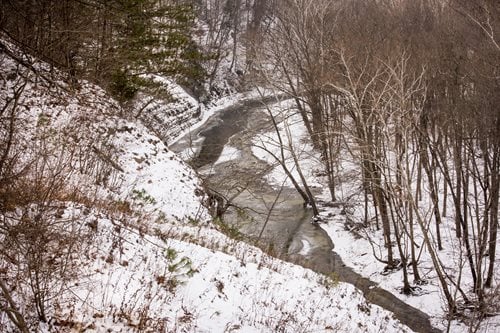 A serene river flows through a snowy forest, surrounded by tall trees blanketed in white snow.